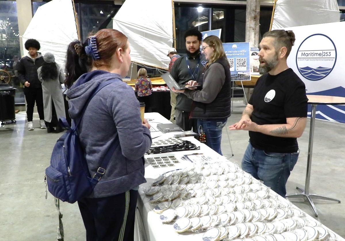 A man standing behind a table of cookies talks to two women at an event.