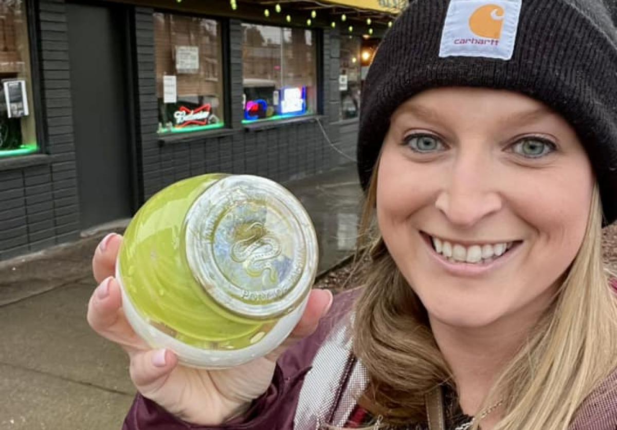 A woman in a black beanie smiles while holding up a round, lime green trinket