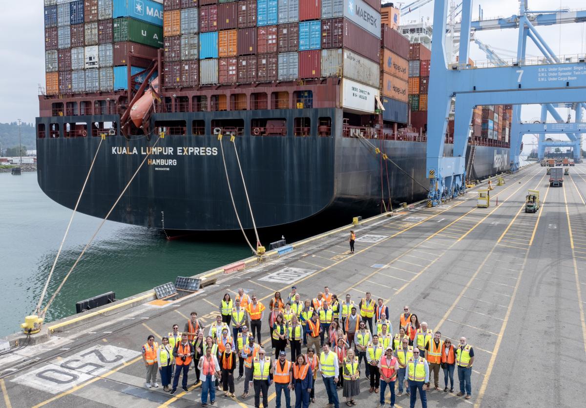 Aerial shot of a group of people standing on a port terminal in front of a container ship.