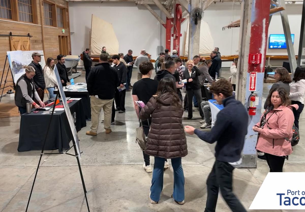 A group of people walk through an event filled with display booths. 