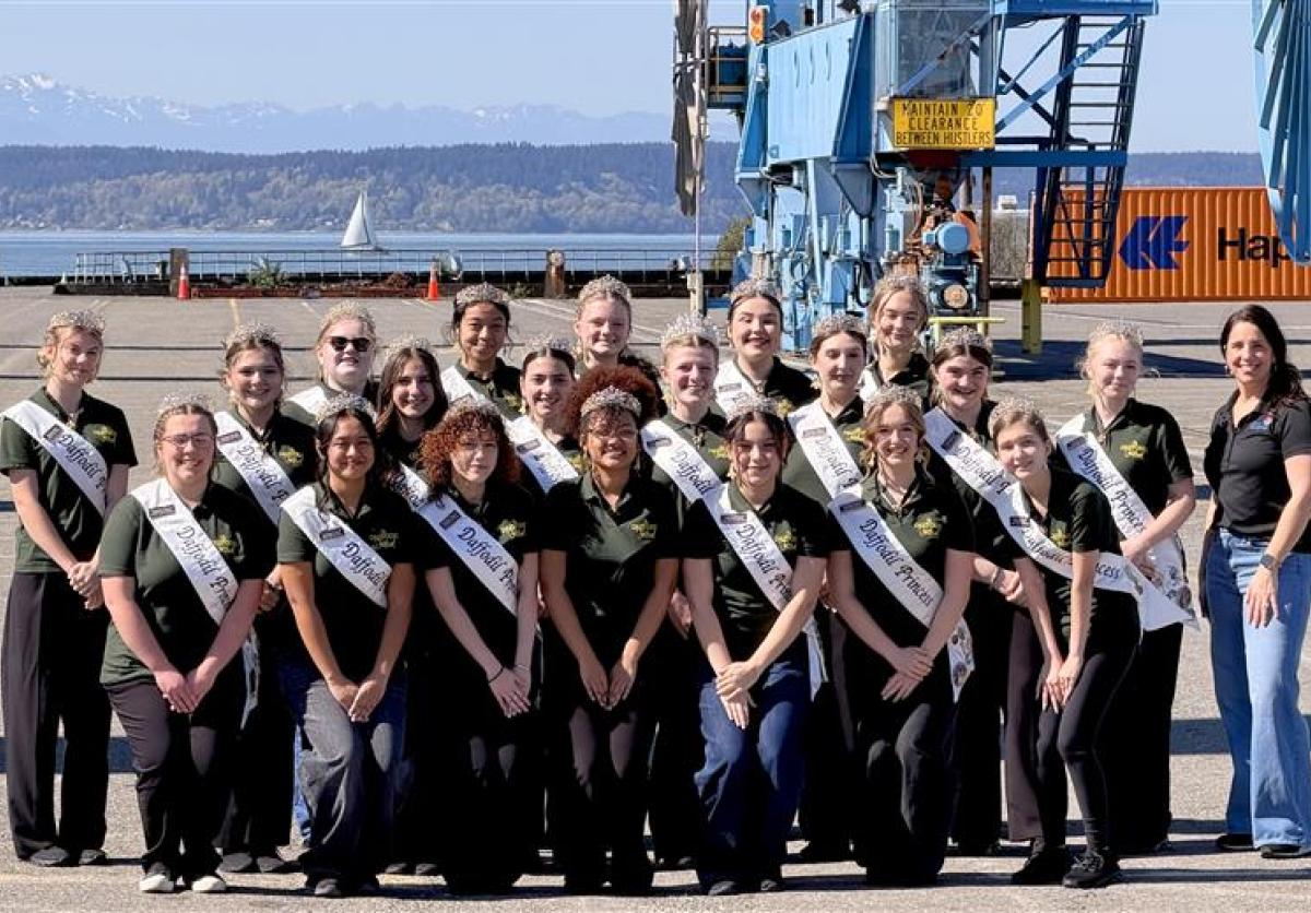 A group of Daffodil Festival princesses post on a port terminal with an employee.